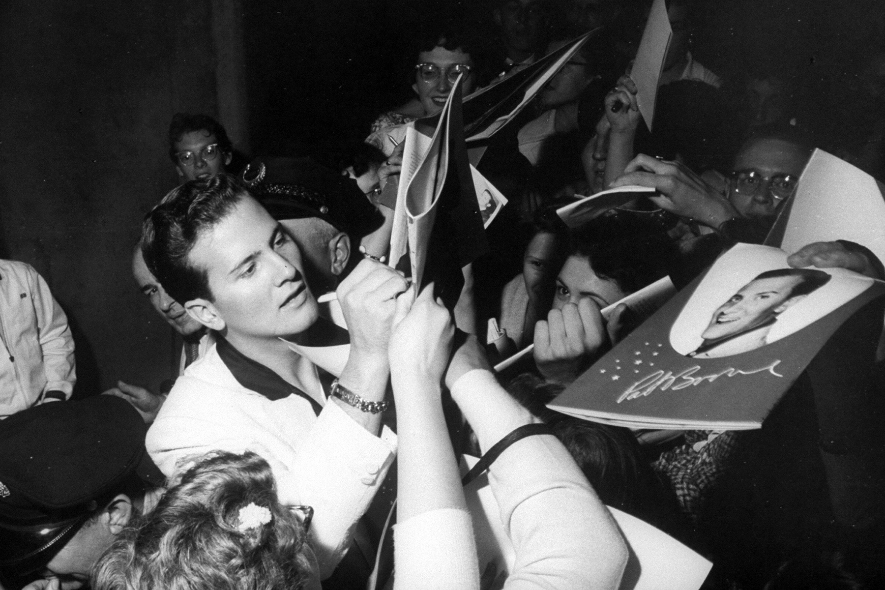 Singer Pat Boone signing his autograph on concert programs which feature his picture on cover, held up by enthusiastic fans who crowd around after his performance at auditorium. (Photo by Time Life Pictures/Pix Inc./The LIFE Picture Collection via Getty Images)